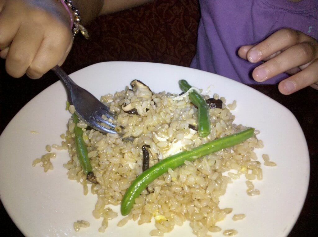 Child eating brown rice with mushrooms and green beans on a plate. 