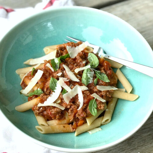 Spaghetti sauce over pasta topped with shredded cheese in a blue bowl.