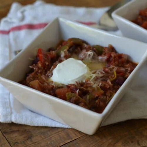 Slow Cooker Red and Green Chili in a white bowl topped with sour cream and cheese